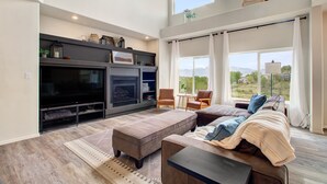 A spacious living room with a large TV, comfortable seating, and a balcony with a view. - Creekside Mountain View Retreat, Hot Tub, Sleeps 14, 6 Kings, 5 bathrooms (Colorado Springs)