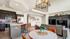 A modern kitchen with stainless steel appliances, a dining area with a round table and chairs, and a cozy living space with a sofa and a fireplace. - Creekside Mountain View Retreat, Hot Tub, Sleeps 14, 6 Kings, 5 bathrooms (Colorado Springs)