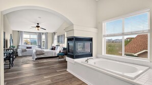 A spacious bedroom with a large bed, a sitting area with a desk, and a view of the outside. - Creekside Mountain View Retreat, Hot Tub, Sleeps 14, 6 Kings, 5 bathrooms (Colorado Springs)