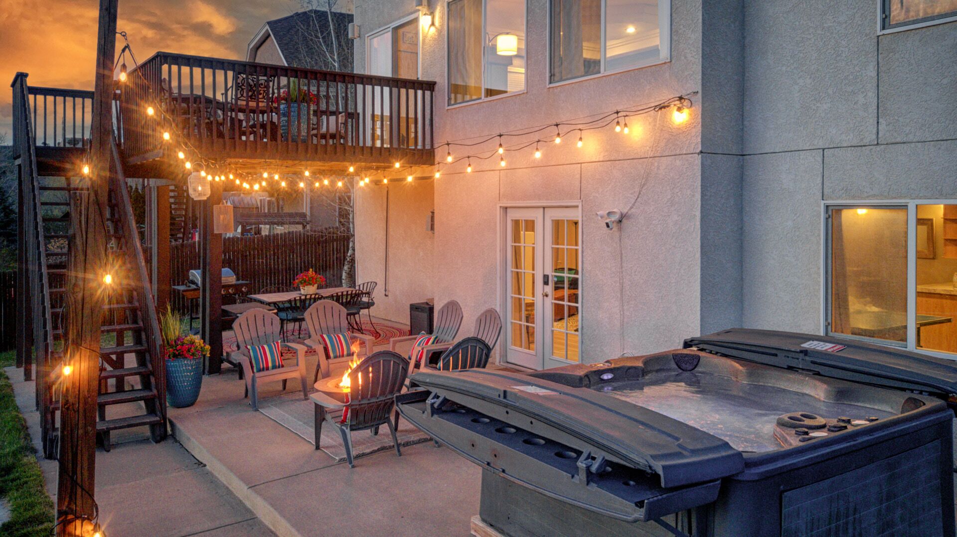 A backyard with a hot tub, outdoor seating, and string lights.