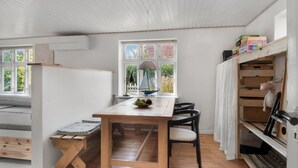 Een gezellige kamer met een houten tafel, stoelen, een bank en een raam met uitzicht op groen.
