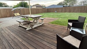 A wooden deck with a picnic table and chairs, a large umbrella, and a grassy yard in the background. - Dolphin Place | Spacious home/ backyard and centrally located | 3 Bed | 2 Bath | (Corpus Christi)