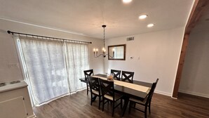 A dining area with a wooden table and chairs, a chandelier, and a window with curtains. - Dolphin Place | Spacious home/ backyard and centrally located | 3 Bed | 2 Bath | (Corpus Christi)