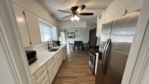 A kitchen with white cabinets, a stainless steel refrigerator, a microwave, and a ceiling fan. - Dolphin Place | Spacious home/ backyard and centrally located | 3 Bed | 2 Bath | (Corpus Christi)