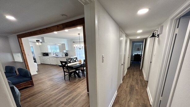 A modern kitchen with white cabinets, a dining area with a wooden table and chairs, and a hallway with wooden flooring and white walls. - Dolphin Place | Spacious home/ backyard and centrally located | 3 Bed | 2 Bath | (Corpus Christi)