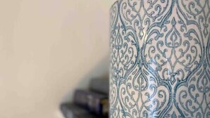 A decorative ceramic container with intricate blue patterns on a beige shelf.