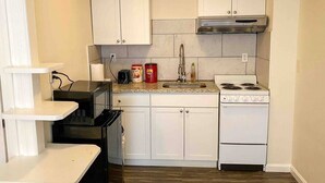 A compact kitchen with white cabinets, a gas stove, a microwave, and a stainless steel range hood.