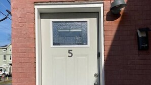 A white door with the number 5, a small window with frosted glass, and a wall-mounted light fixture.