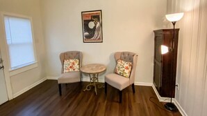 Une pièce comprenant deux fauteuils, une petite table ronde, un lampadaire et un tableau accroché au mur.