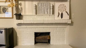 A white brick fireplace with a mantel shelf displaying a dreamcatcher, a framed abstract art piece, and a potted orchid. - Stylish Studio Apartment in Downtown Lexington (Lexington)