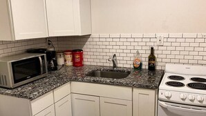 A kitchen with white cabinets, a granite countertop, a microwave, a sink, a stove, and various kitchen items. - Stylish Studio Apartment in Downtown Lexington (Lexington)