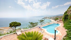Zona de piscina amb vistes al mar, un solàrium amb rajoles i una barana.