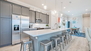 A modern kitchen with grey cabinets, stainless steel appliances, and a central island with bar stools. - Coral Sunset: Free golf cart, 2min to beach, Heated pool steps away, Bunk rooms (Miramar Beach)