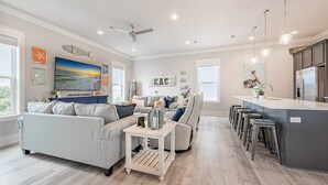 A spacious living room with a gray sofa, a coffee table, and a dining area with bar stools. - Coral Sunset: Free golf cart, 2min to beach, Heated pool steps away, Bunk rooms (Miramar Beach)