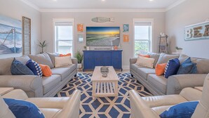 A living room with two grey sofas, a coffee table, and a large TV screen. - Coral Sunset: Free golf cart, 2min to beach, Heated pool steps away, Bunk rooms (Miramar Beach)