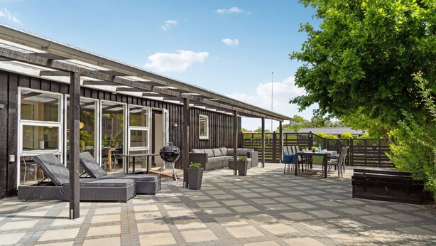 Une terrasse avec des meubles d’extérieur, un barbecue et un espace salon abrité.