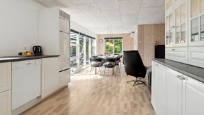 Une cuisine moderne avec des meubles blancs, un plancher en bois et un coin repas doté de chaises noires.