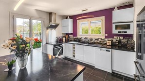 A modern kitchen with white cabinets, a black countertop, and a purple accent wall. - Nice home in Sérignan (Sérignan)