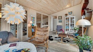 A cozy, rustic interior with a wooden ceiling, a large white chandelier, leather furniture, and a cowhide rug.