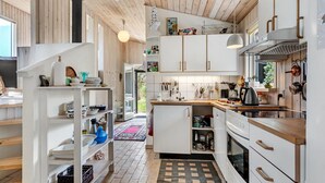 A modern kitchen with white cabinetry, a wooden countertop, and a built-in oven. There is a hanging light fixture and a window providing natural light.
