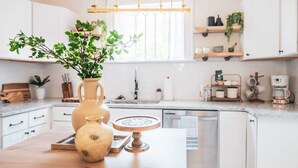 Une cuisine moderne avec des meubles blancs, un plan de travail en bois, un évier et une fenêtre équipée de stores.