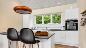 Cocina moderna con una isla central, dos taburetes negros, horno empotrado y ventana con vistas a zonas verdes.