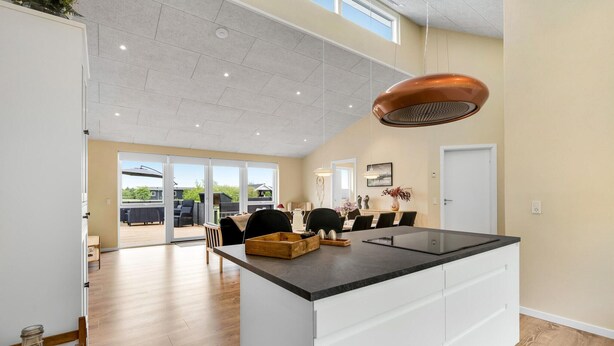 Una cocina amplia con una isla grande, puertas de vidrio correderas que dan a un patio exterior y un techo alto con iluminación empotrada.