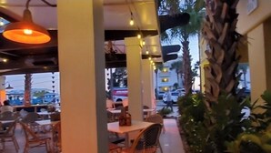 Un café en plein air avec des tables et des chaises, des guirlandes lumineuses et des palmiers.