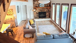 Ein geräumiges Wohnzimmer mit Kamin aus Stein, einem grauen Sofa und einem Essbereich mit Tisch und Stühlen.