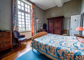 A bedroom with a bed, dresser, chair, and a large window with curtains.