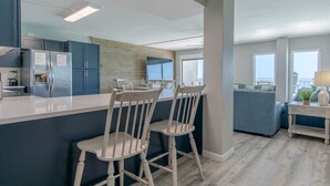 A modern kitchen with blue cabinets, a white island, and wooden chairs. - Summit Penthouse 3BR 3BA VERY RARE!! (Panama City Beach)