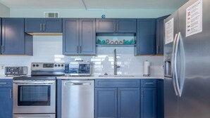 A modern kitchen with dark blue cabinets, stainless steel appliances, and a tiled backsplash. - Summit Penthouse 3BR 3BA VERY RARE!! (Panama City Beach)