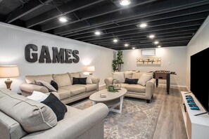 A modern living room with two sofas, a coffee table, and a foosball table.