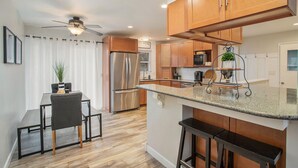 A modern kitchen with wooden cabinets, a stainless steel refrigerator, and a bar area. - Poolside Playhouse: Hot Tub, Firepit & Games (Stevensville)