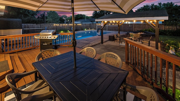 An outdoor patio with a pool, wooden deck, and seating area. - Poolside Playhouse: Hot Tub, Firepit & Games (Stevensville)
