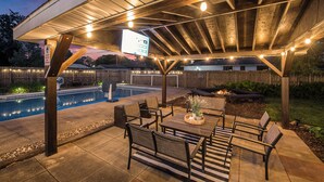 A covered outdoor patio with a pool, seating area, and a sign. - Poolside Playhouse: Hot Tub, Firepit & Games (Stevensville)