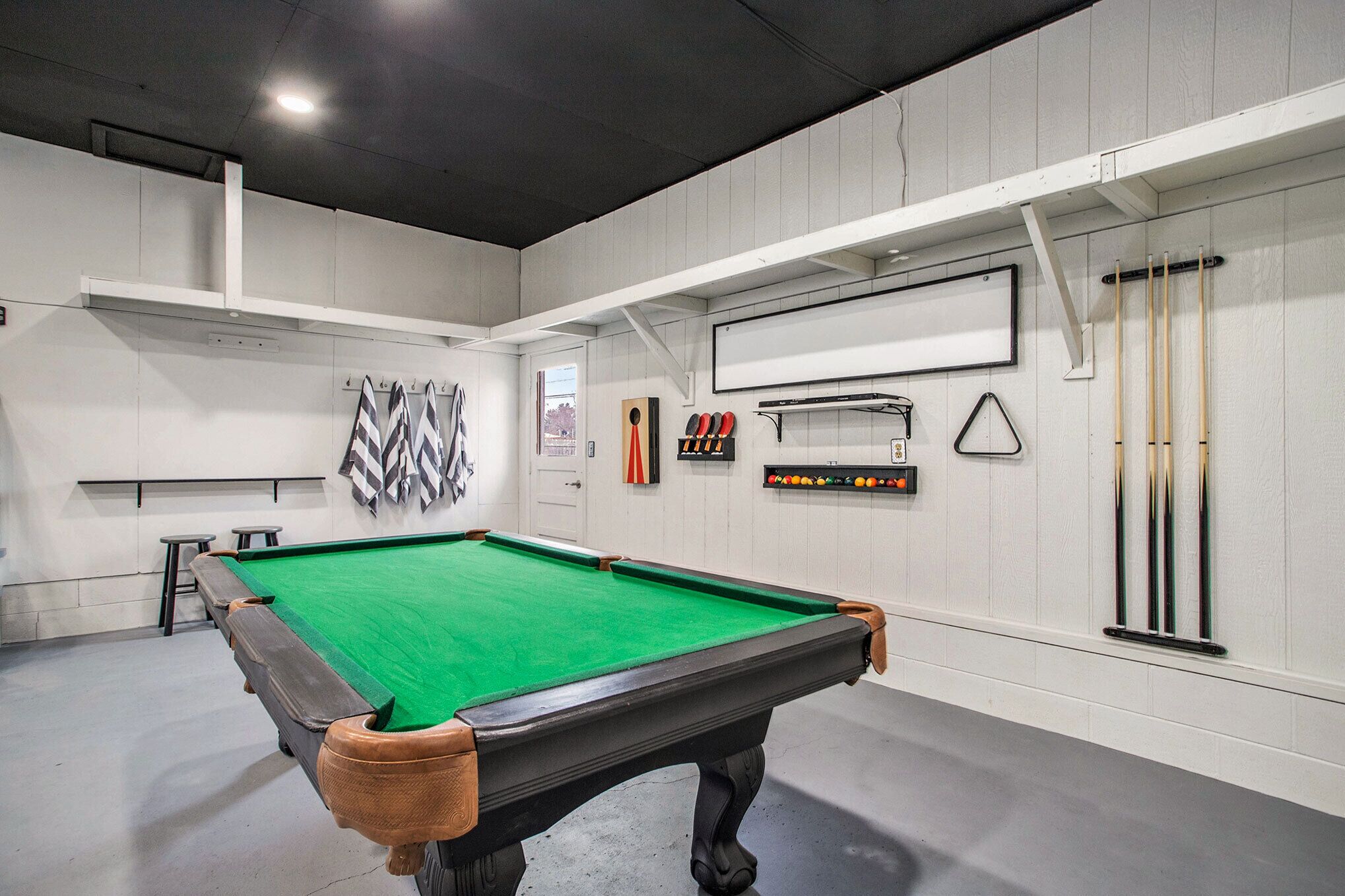 A pool table with a green felt surface, surrounded by white walls and a ceiling with recessed lighting.
