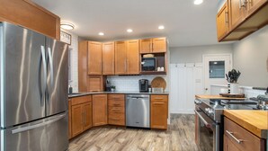 A modern kitchen with wooden cabinets, stainless steel appliances, and a tiled backsplash. - Poolside Playhouse: Hot Tub, Firepit & Games (Stevensville)
