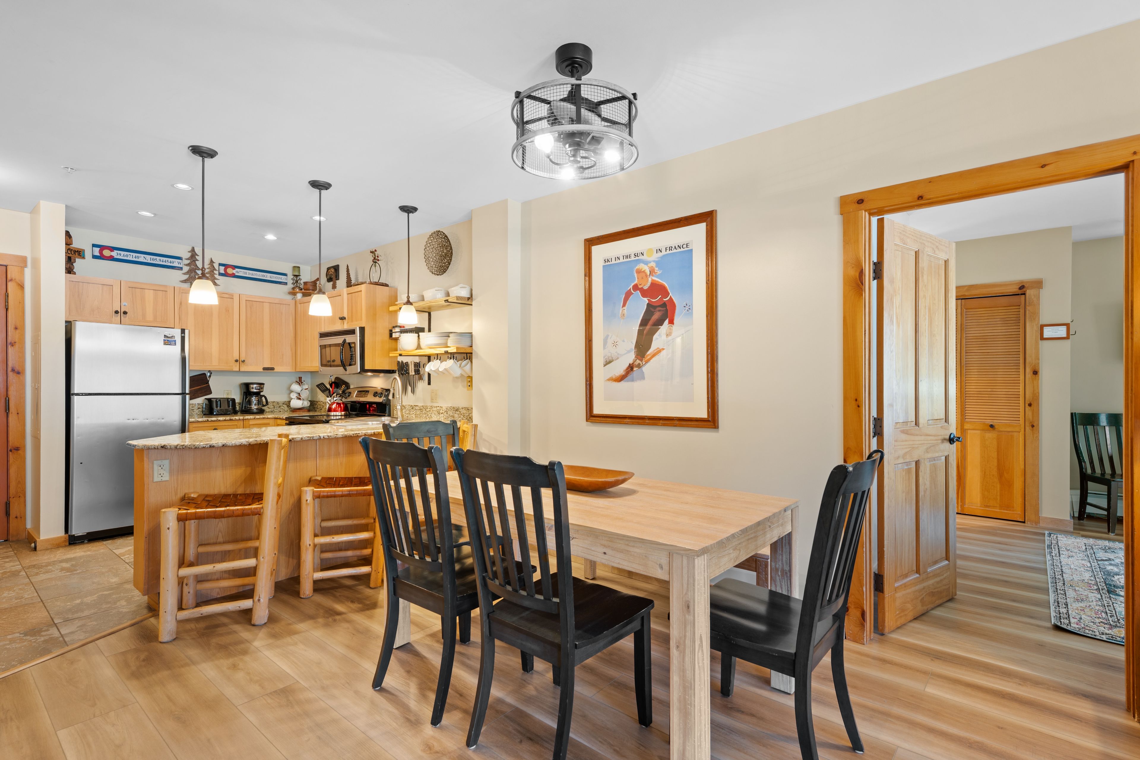 A modern kitchen with wooden cabinets, a stainless steel refrigerator, and a dining area with a wooden table and chairs.