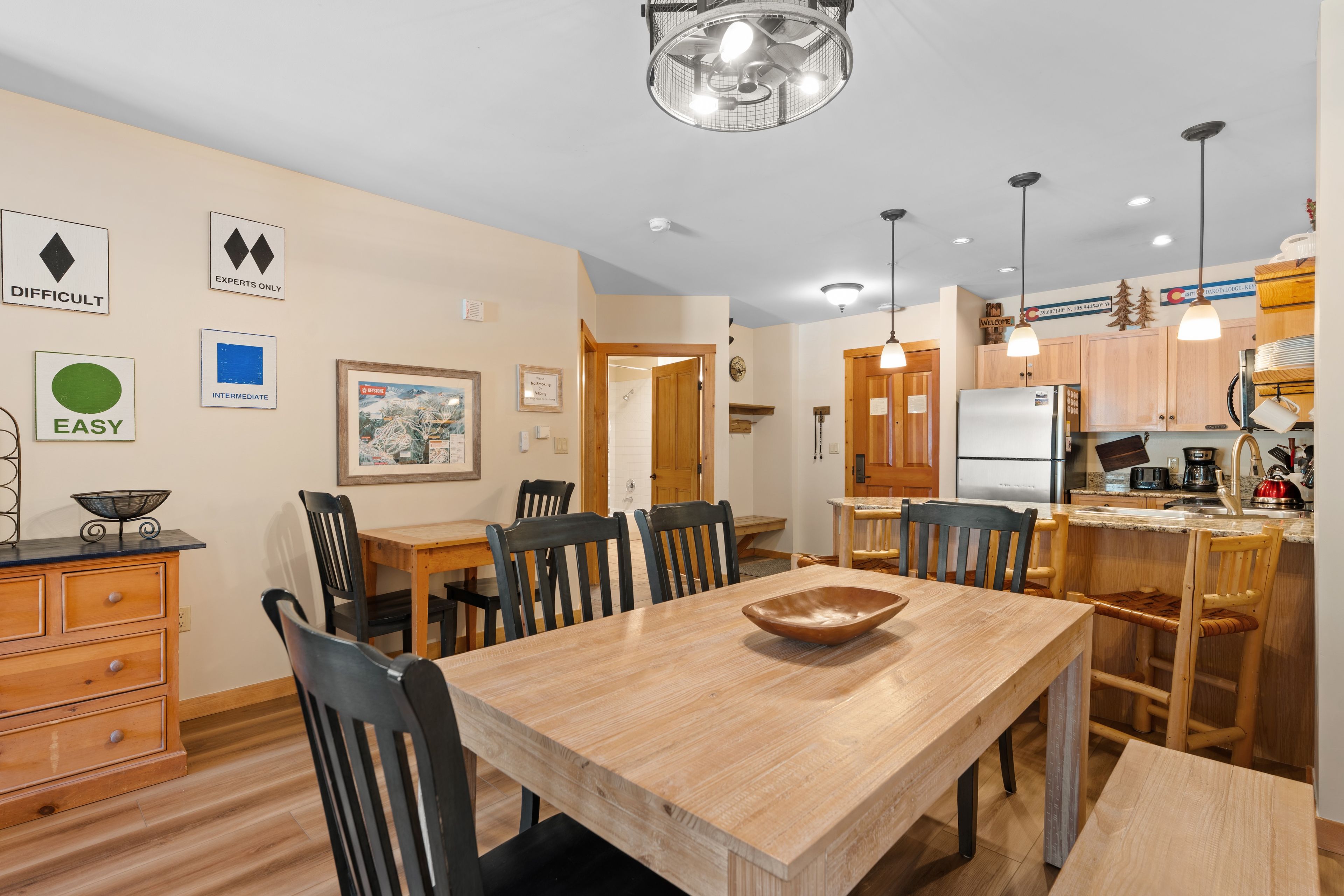 A modern kitchen with wooden cabinets, a stainless steel refrigerator, and a dining area with a wooden table and chairs.