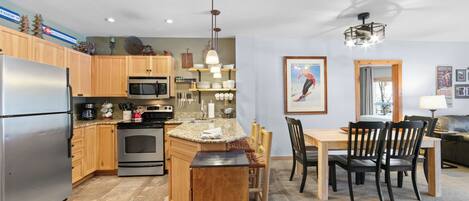 A modern kitchen with wooden cabinets, stainless steel appliances, and a dining area with a table and chairs.