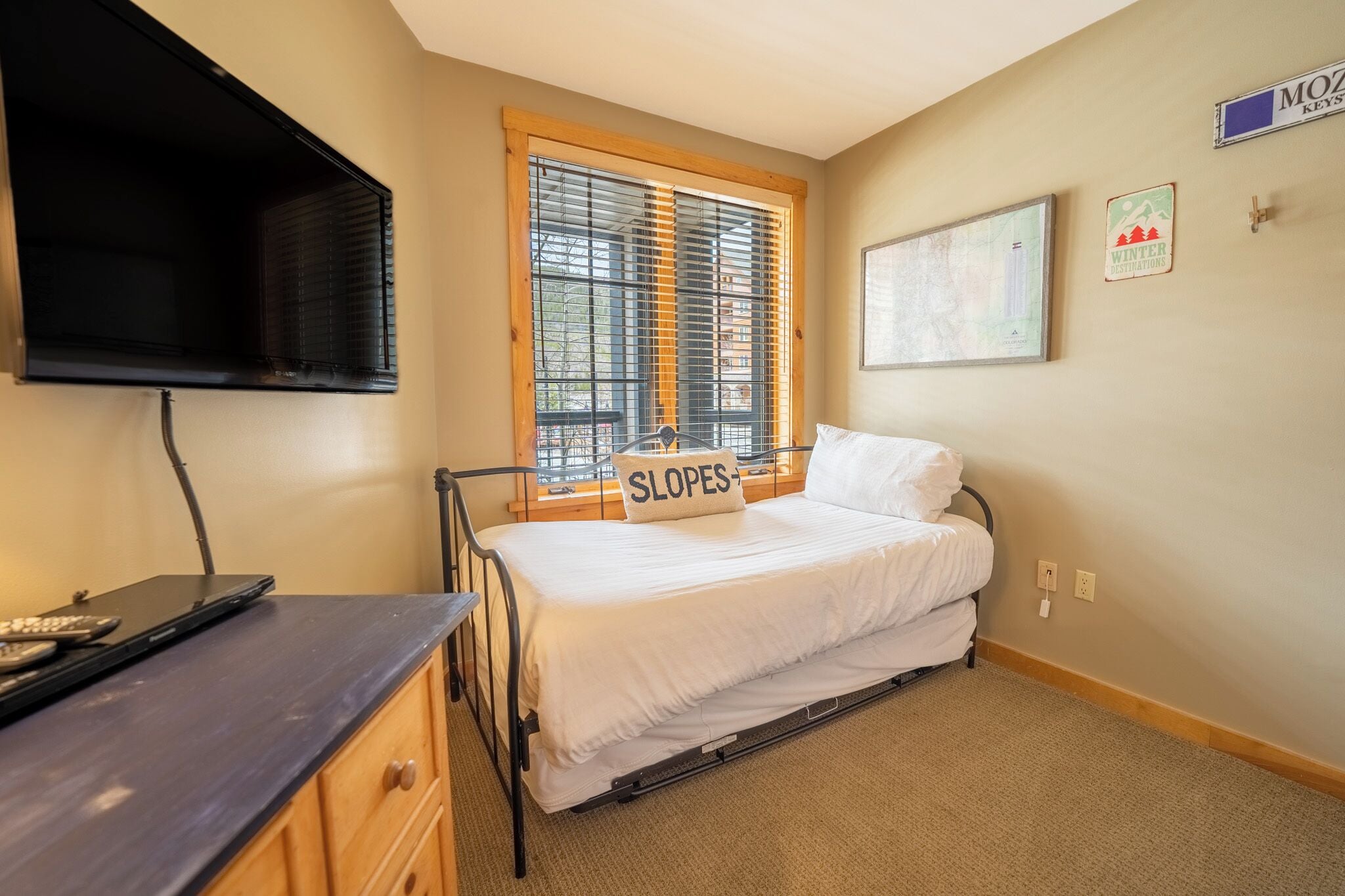 Une petite chambre à coucher avec un lit, un bureau et une fenêtre équipée de stores.