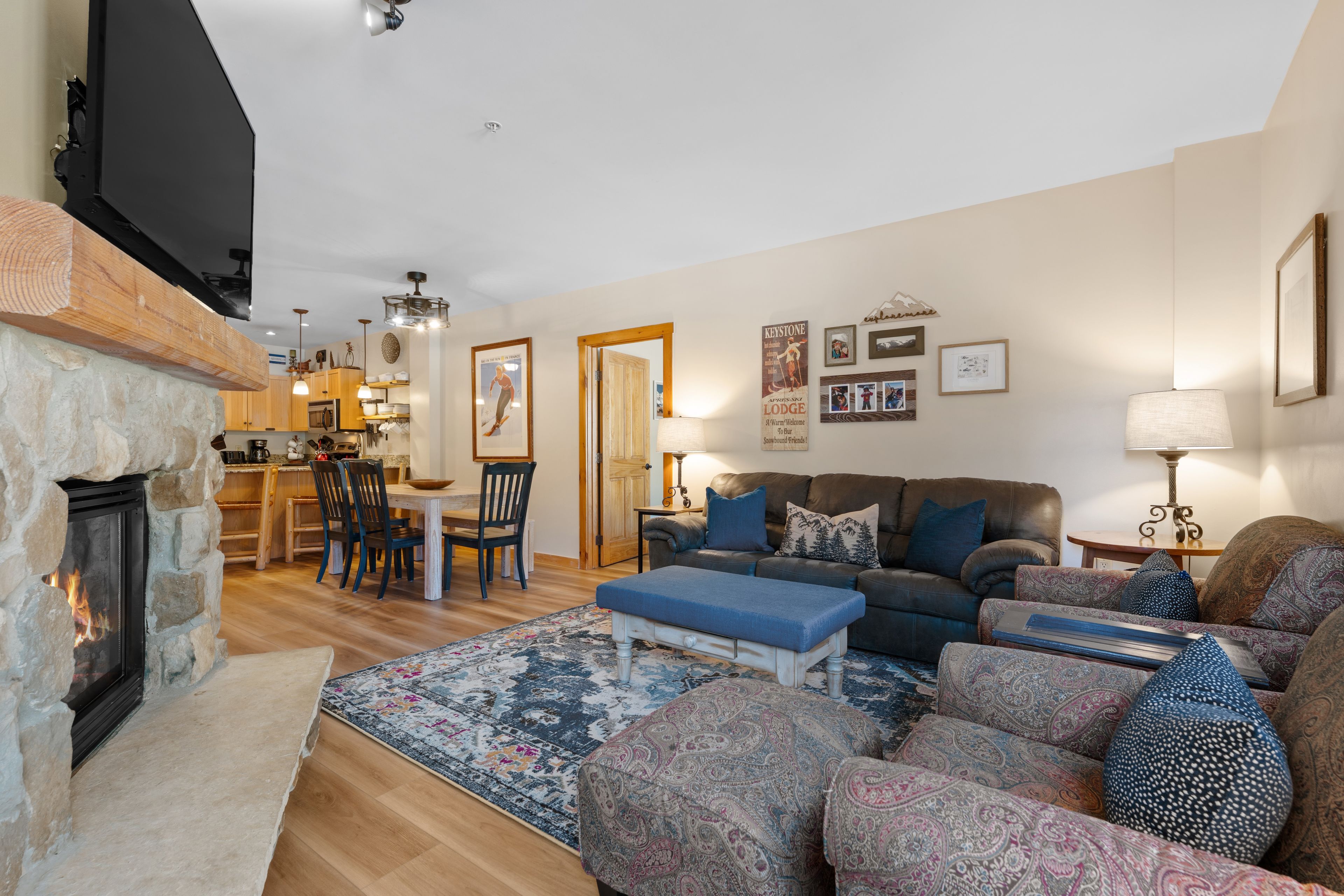A living room with a fireplace, a sofa set, a dining area, and a kitchen visible through an open door.