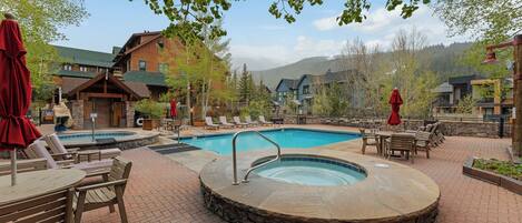 A pool area with lounge chairs and a hot tub, surrounded by buildings and trees.