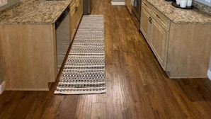 Une cuisine étroite avec des meubles en bois, un îlot central et un tapis à motifs.