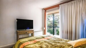 Een hotelkamer met een bed, een televisie op een houten standaard en een balkon met gordijnen.