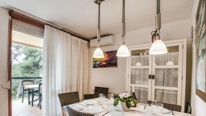 Een eethoek met een tafel gedekt voor vier personen, twee hanglampen, een schilderij aan de muur en uitzicht op de omgeving.