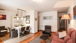 Een woonkamer met een eetgedeelte, een zwarte bureaustoel, een roze bank en een radiator.