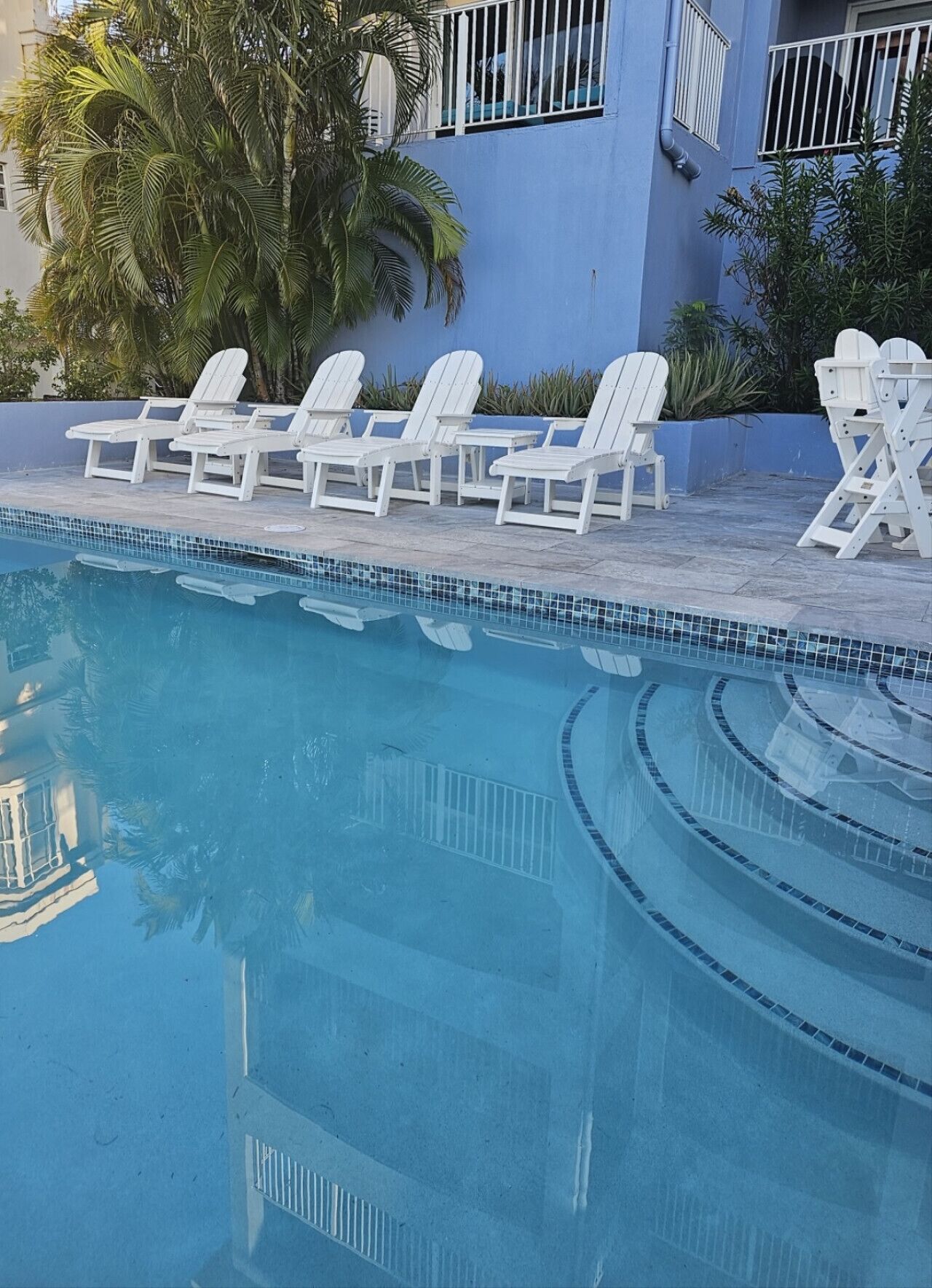 A swimming pool with white lounge chairs and a blue building in the background.