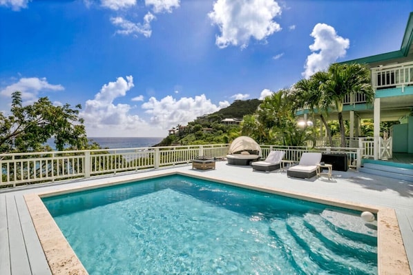 A pool area with lounge chairs and a view of the ocean.